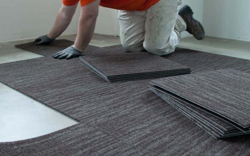 Installer placing brown carpet tiles